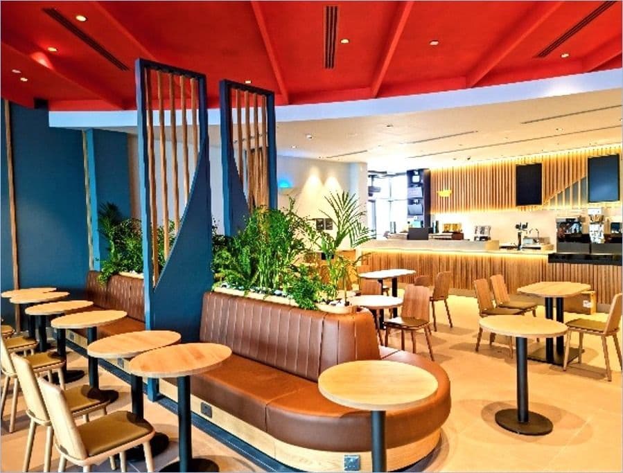 Café seating with leather banquettes, planters and timber screens under a red ceiling