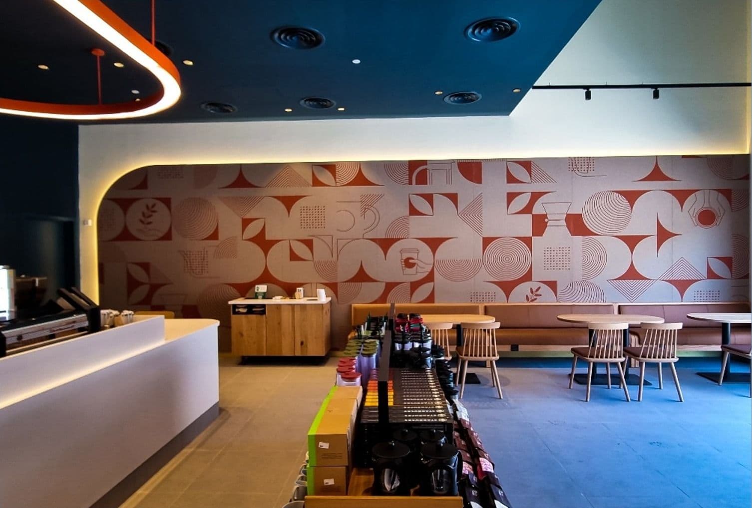 Café counter and seating in front of a red geometric patterned feature wall with curved lighting